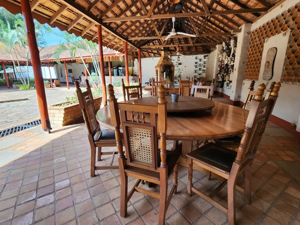Open-air terrace dining area with a round wooden table under a thatched roof at Masindi Hotel
